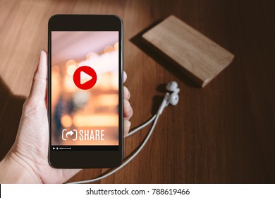 Hand Holding Mobile Watching Viral Video Advertising On Phone Screen At Blur Wood Table,share Video On Social Media Concept,Digital Marketing Strategy
