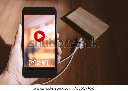 Hand holding mobile watching viral video advertising on phone screen at blur wood table,share video on social media concept,Digital marketing strategy
