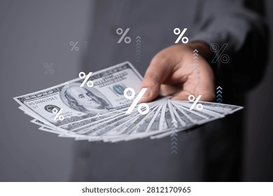 Hand holding multiple US dollar banknotes with percentage symbols overlay, representing interest rates, inflation, financial growth, investment profits, banking, lending, rising costs, modern economic