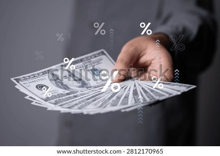 Hand holding multiple US dollar banknotes with percentage symbols overlay, representing interest rates, inflation, financial growth, investment profits, banking, lending, rising costs, modern economic