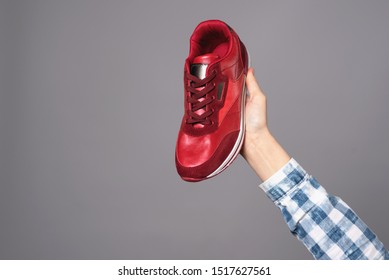 Hand Holding New Red Sport Sneaker Isolated On Gray Background.