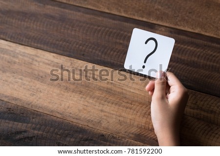 hand holding a note written a question mark on a wooden table background