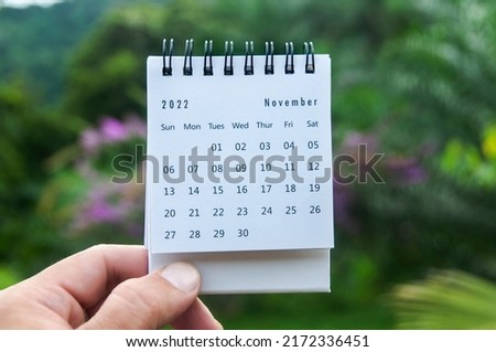 Hand holding November 2022 calendar with copy space and nature background.