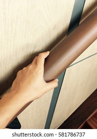 The Hand Holding On To A Wooden Banister. Closeup Of Senior Using The Wooden Railing Of Stairs To Go Upstairs At Home.