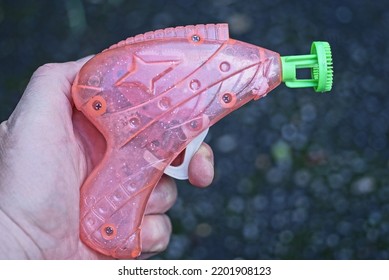 Hand Holding One Pink Plastic Gun Toy On Gray Background