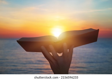 Hand Holding Open Bible Book Up To The Sun Light.