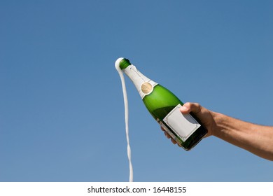 Hand Holding An Open Bottle Of Champagne On A Background Of The Blue Sky