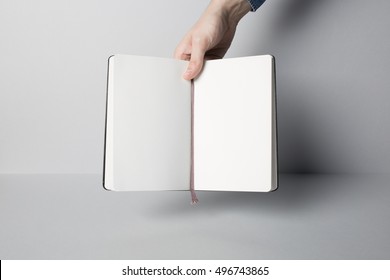 Hand holding opened notebook, blank paper Mock-up.