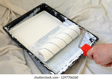 Hand Holding A Paint Roller In A Tray Of Paint Sat On A Decorators Dust Sheet.