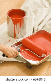 Hand Holding Paint Roller In Tray With Painting Supplies On Drop Cloth.