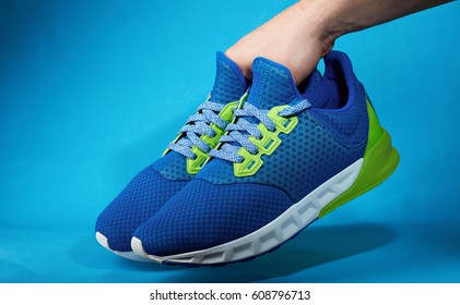 Hand Holding Pair Of New Running Shoes Isolated On Blue Background. Become Sporty Life