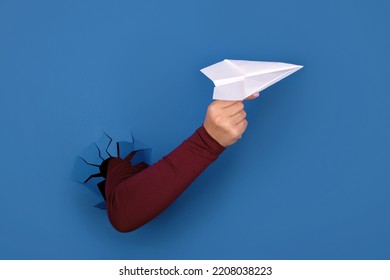 Hand Holding Paper Airplane Over Blue Background