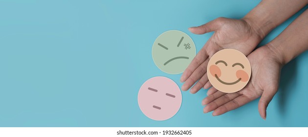 Hand Holding Paper Cut Happy Smile Face On Blue Background, Positive Thinking, Mental Health Assessment , World Mental Health Day Concept