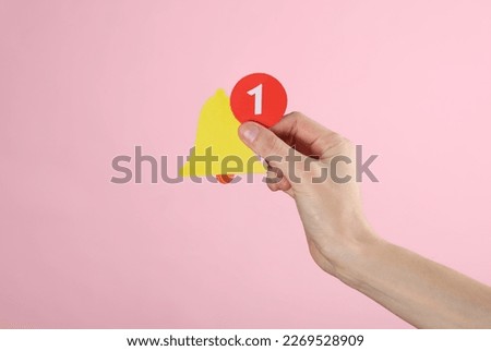Hand holding paper cut notification bell on pink background. Social media, message, sms, subscribe notice alert and reminder.