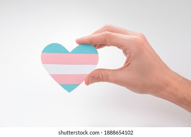 Hand Holding A Paper Heart With Transgender Flag On White Background. Beautiful Art To Express Pride Of Trans People.