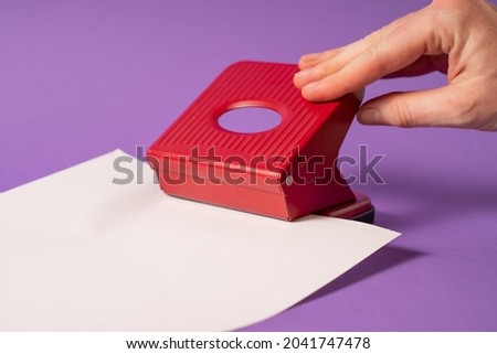 Hand holding paper hole puncher on violet background. Red office paper hole punch. The girl makes paper holes with punch