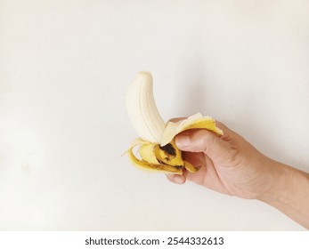 A hand is holding a peeled banana. Close up shot.