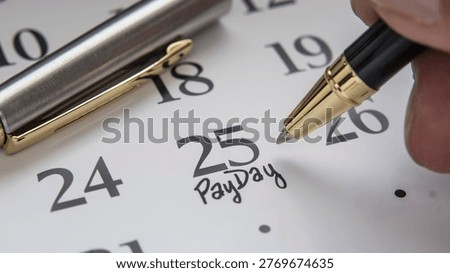 A hand holding a pen points to the 25th on the calendar. The 25th of the calendar is marked as payday.