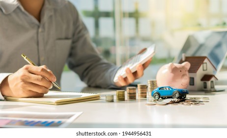 Hand Holding A Pen With Stacked Coins And A Wooden House Model With A Car Or Real Estate Brokerage Idea. Insurance Or Real Estate Loans Business House Investment Ideas