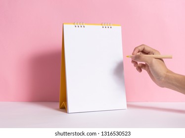 Hand holding pencil for writing marking on mockup paper spiral calendar on pink background.   - Powered by Shutterstock