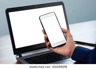 Hand holding phone mobile phone or smartphone mockup screen with laptop computer on workplace 