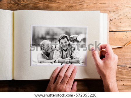 Hand holding photo album with pictures of senior couple. Studio