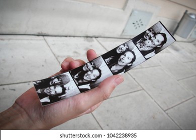Hand holding a Photo booth strip with the photos of a young couple