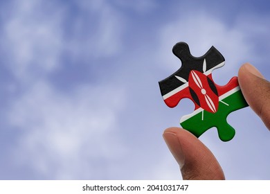 Hand holding piece of jigsaw puzzle with flag of Kenya. Jigsaw puzzle of Kenya flag on sky background.