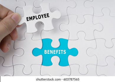 Hand holding piece of jigsaw puzzle with words Employee Benefits.