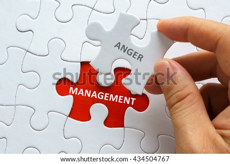 Hand holding piece of jigsaw puzzle with word ANGER MANAGEMENT.