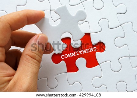 Hand holding piece of puzzle with word COMMITMENT