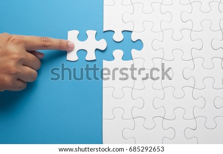 Hand holding piece of white puzzle on blue background. Business and team work concept. 