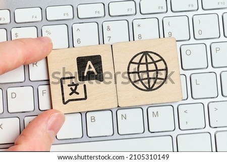 Hand holding a piece of wood with a symbol of a translator on the keyboard.