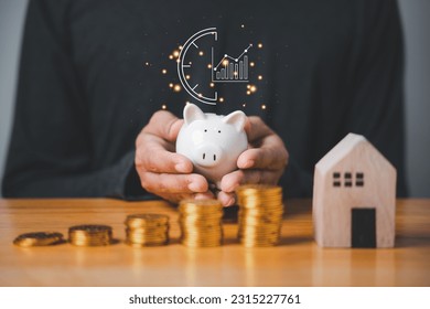 A hand holding a piggy bank with coins stacked beside it, symbolizing idea of saving and investing money. The concept of financial planning and wealth management is important for economic stability. - Shutterstock ID 2315227761