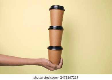 Hand Holding Pile Of Creative Disposable Cup Over Yellow Background - Powered by Shutterstock