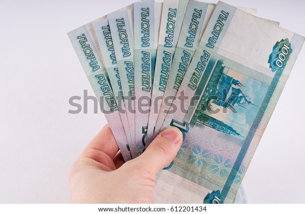 A hand holding a pile of\
thousand-dollar ruble notes. Russian currency on a white\
background.