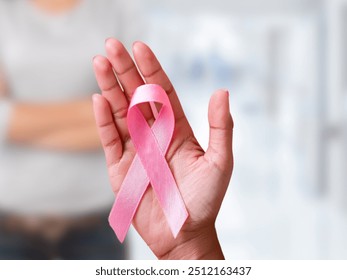 A hand holding a pink ribbon symbolizing breast cancer awareness, radiating hope and support. - Powered by Shutterstock