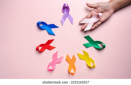 Hand holding pink ribbon which is among colorful ribbons on pink background, cancer awareness, World cancer day, National cancer survivor day, world autism, supported living and illness. - Powered by Shutterstock