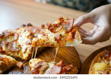 Hand holding pizza slice from tray. it is an Italian fast food consisting of a flat round dough topped with tomato sauce. Then cooked by baking in the oven.                                - Powered by Shutterstock