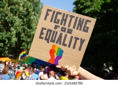 Hand holding placard sign Fighting for Equality with rainbow flag fist, during LGBT Pride Parade. Crowd of people at equality march to support and celebrate LGBT+, LGBTQ gay and lesbian community. - Powered by Shutterstock