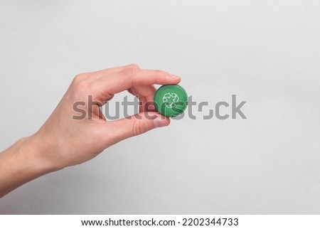 Hand holding Plastic bottle cap with circular recycling symbol on gray background. Round recycle, eco concept