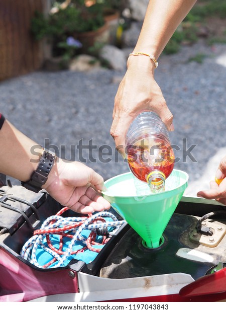 Hand holding plastic bottle of\
fuel and filling to motorcycle at local gas station in\
Thailand.