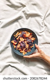 Hand Holding A Plate With Crunchy Vegetable Chips On The Table With Linen Tablecloth. Veggie Snack. Alternative Healthy Eating. Proper Nutrition. Dehydrated Vegetables