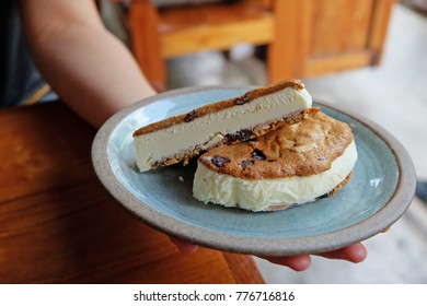 Hand Holding Plate Of Vanilla Ice Cream In Chocolate Chip Sandwich