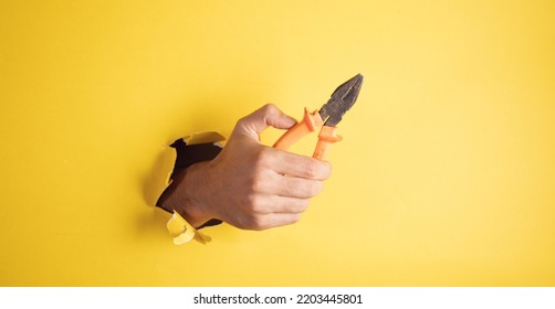 Hand Holding Pliers On Yellow Background