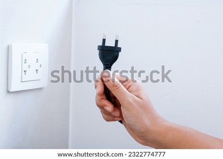 Hand holding plug prepares to  connect a power plug into a electrical outlet on a wall, power outlet socket, power saving concept, energy saving, energy conservation.