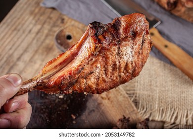 Hand Holding Pork Prime Rib Roast By The Bone And On Wooden Board.