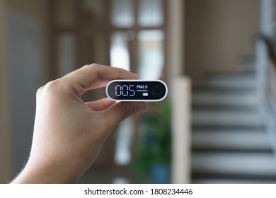 Hand Holding Portable Air Quality Detector With Indoor Background. 