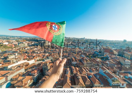 hand holding portuguese flag on aerial view of historic center of Porto in Portugal from Clerigos Tower, one of the landmarks and icon of Oporto. Urban cityscape with blue sky