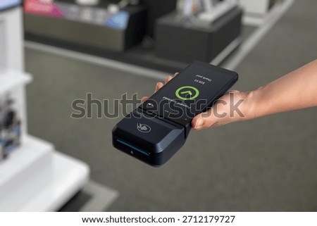 Hand holding POS terminal in electronics store, showing payment approved screen during digital checkout and cashless transaction process